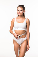 Young woman in her underwear with a measuring tape wrapped around her stomach against a white...
