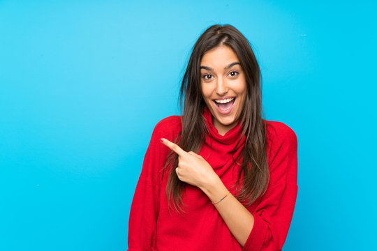 Young woman with red sweater over isolated blue background pointing finger to the side