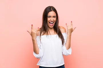 Fotobehang Young woman over isolated pink background making rock gesture © luismolinero