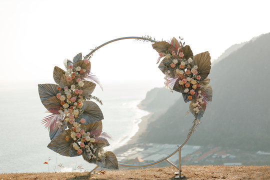 Wedding ceremony on the  cliff with sea view. Wedding round arch decorated with beautiful colorful  flowers on the sea cliff Ocean on background, sunset time