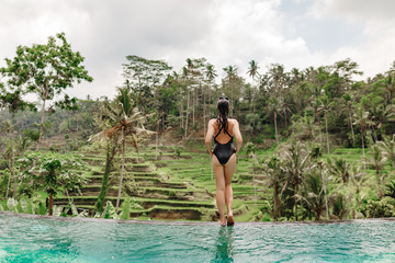 Young girl stand on the edge of infinity pool with a view on rice terrace. Travelling to Ubud, Bali, Indonesia