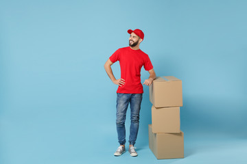 Delivery man in red uniform isolated on blue background, studio portrait. Male employee in cap...