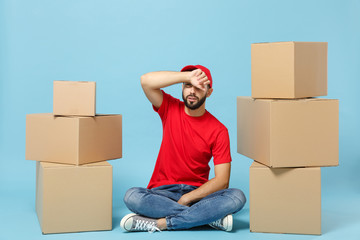 Delivery sad man in red uniform isolated on blue background, studio portrait. Male employee in cap t-shirt print working as courier dealer hold empty cardboard box. Service concept. Mock up copy space