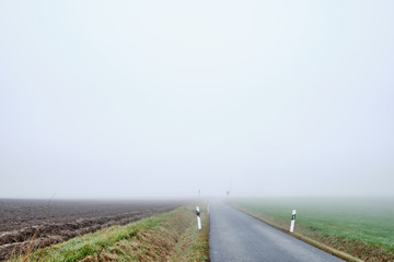 Countryside road to nowhere -  narow street with diminishing perspektive leading into the fog. Seen in Germany near Oedenberg, Bavaria in October.