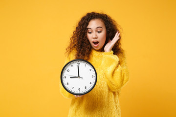 Shocked young african american girl in fur sweater posing isolated on yellow orange wall...