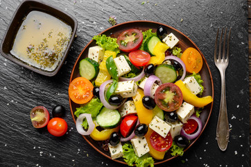 Top view at Mediterranean diet dish greek salad on slate tray with sauce aside