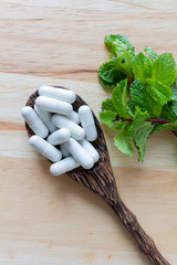Mint and capsule medicine on pattern wooden background,