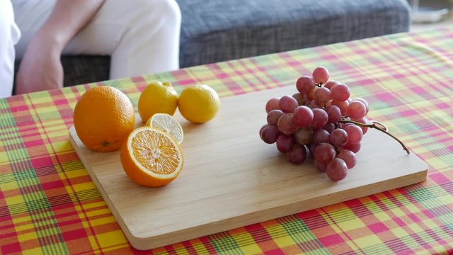 unrecognizable Man with white pant taking a glass of orange juice on Table with madras table clothe, wooden plate fresh organic orange, lemon and grapefruit.