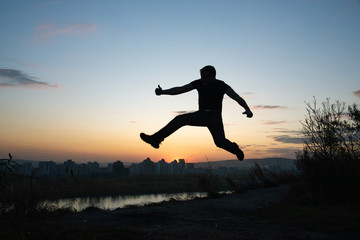 Silhouette of a jumping happy man on the background of the city and summer sunset