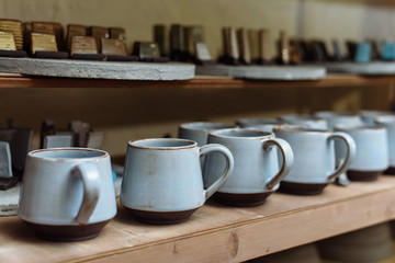 glazed ceramic dishes stand on a shelf in the workshop shelving with handmade ceramic and clay mugs