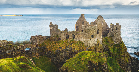 Ruined Ancient Castle at Seaside Nothern Ireland. Remains of Medieval Building, Cloudy Sky and Ocean on Background. Beautiful Landscape Scenery and Architecture Countryside Aerial View Photo