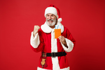 Elderly gray-haired mustache bearded Santa man in Christmas hat isolated on red background. New Year 2020 celebration holiday concept. Mock up copy space. Holding passport ticket doing winner gesture.