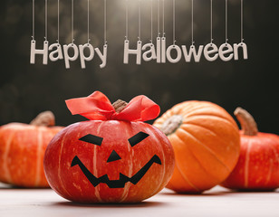 Happy Halloween. Set of pumpkins, one with painted face and  ribbon bow on  ponytail. Dark bokeh background.