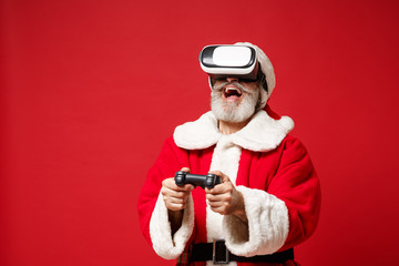Elderly gray-haired mustache bearded Santa man in Christmas hat posing isolated on red background. Happy New Year 2020 celebration holiday concept. Mock up copy space. Wearing headset, hold joystick.