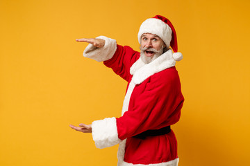 Fototapeta na wymiar Elderly gray-haired bearded mustache Santa man in Christmas hat posing isolated on yellow background. New Year 2020 celebration concept. Mock up copy space. Demonstrating size with vertical workspace.