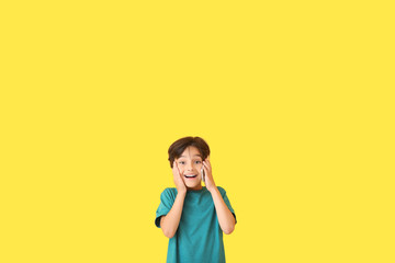Surprised little boy talking by mobile phone on color background