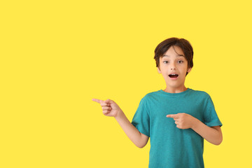 Surprised little boy pointing at something on color background