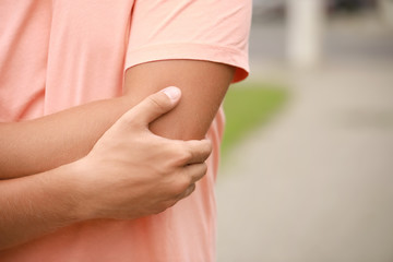 Young sporty man suffering from pain in elbow outdoors, closeup
