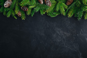 Christmas festive background with christmas tree branches and fir cones on dark concrete stone background.