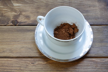 Brown vegetable carob (Ceratonia silica) for making a natural caffeine-free sweet drink. Dry carob powder in a white cup on a wooden background.