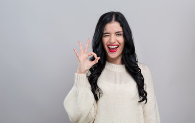 Young woman with ok gesture on a gray background