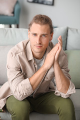 Fototapeta premium Young man with dreadlocks sitting on sofa, casual modern lifestyle, thoughtful and engaged expression