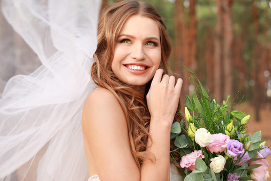 Beautiful young bride with bouquet of flowers outdoors
