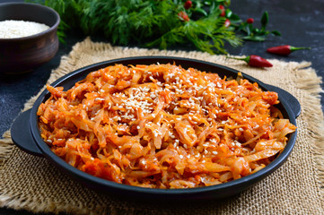 Braised cabbage from tomato sauce in a cast-iron frying pan on a black background. Lenten menu....