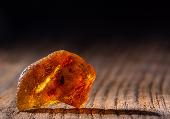 Natural amber. A piece of yellow transparent natural amber on large piece of dark stoned wood. - obrazy, fototapety, plakaty