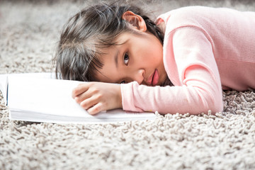 Obraz na płótnie Canvas Cute little girl in casual dress very sleepy after reading book on the carpet in the room.