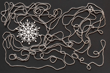 Holiday background , white snowflake and silver decorative beads on black background, flat lay, top view