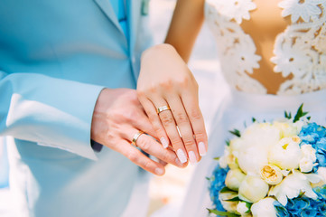 Obraz na płótnie Canvas Hands of newlyweds with beautiful gold rings, close-up. White bridesmaid dress, bouquet, stylish manicure. Perfect wedding ceremony.