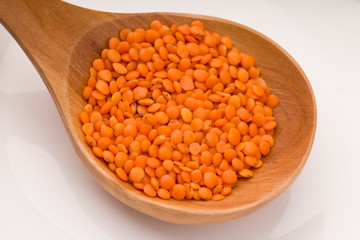 Red lentils in the wooden spoon, isolated on white background.