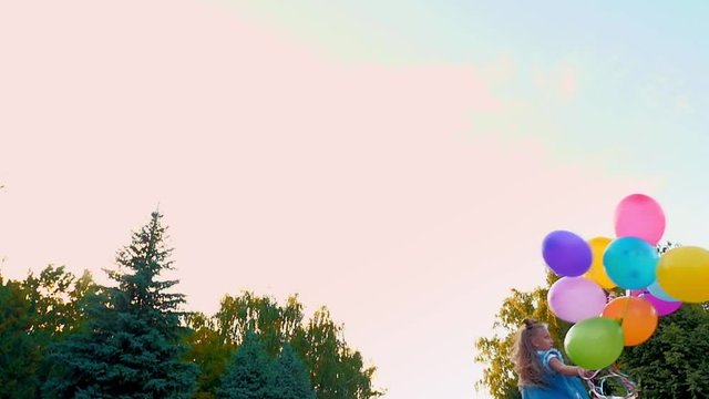 a teenage girl in jeans runs through the park with a large bunch of colorful balloons.
