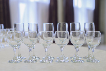 set of empty glass goblets for champagne, wine, water stand in row on table on blurred interior background, horizontal indoors stock photo image