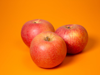 three red and yellow apples isolated on an orange background