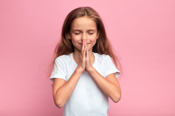 happy adorable girl with closed eyes pressing her palms, kid making a wish. close up portrait, isolated pink background, desire, belief. kid asking God to help her mother , sincere wish, thougth.