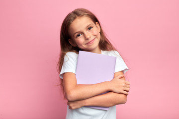 Little beautiful smiling girl holding book, going to school. close up portrait, isolated pink background, childhood. kid hugging a book. lifestyle, interest, hobby, free time, spare time - Powered by Adobe