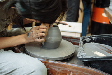 Fototapeta na wymiar The master creates products from gray clay on a potter's wheel. Girl creates a ceramic vase