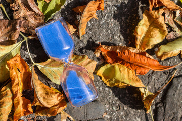 Hourglass on the pavement surrounded by autumn foliage