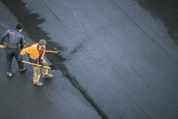 Workers lay a new asphalt coating using hot bitumen. Work of heavy machinery and paver. Top view