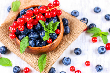 Fresh blueberries and red currants with mint leaves in a wooden bowl on burlap. Diet food, vegan berries