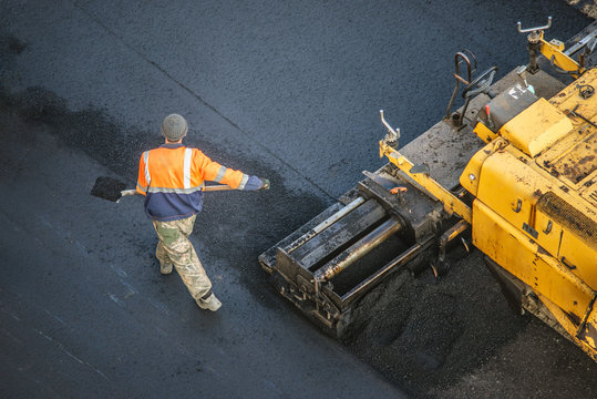 Workers lay a new asphalt coating using hot bitumen. Work of heavy machinery and paver. Top view