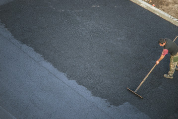 Workers lay a new asphalt coating using hot bitumen. Work of heavy machinery and paver. Top view