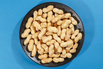 Ripe inshell peanuts on a black plate on a blue background. Healthy eating concept.