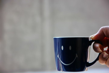 blue ceramic coffee mug with smile pattern in hand  with blur background