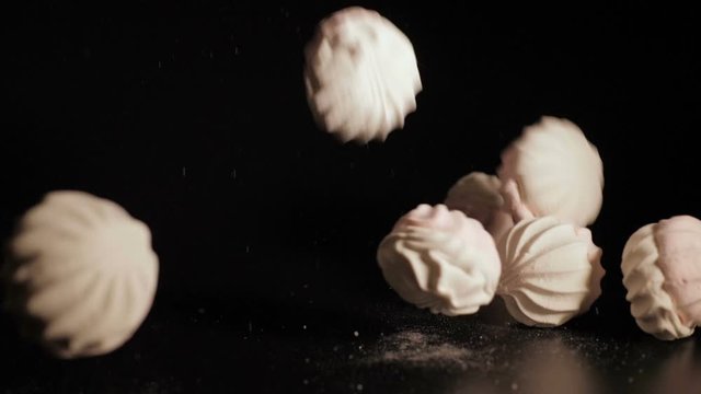Zefir falling close up. White pieces of marshmallow fall in slow motion a black background and bounce off each other. Closeup.