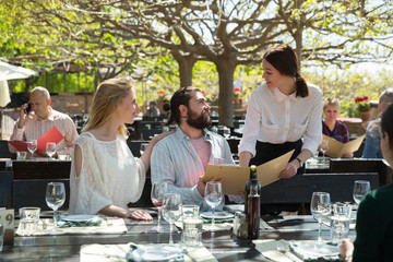 Charming young waiter and couple at open-air restaurant summer