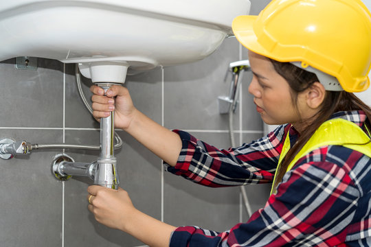 Plumber, plumbing specialist fixing kitchen sink. Young Asian Woman Plumber checking or repairing a leaky drain in bathroom. Construction, engineering, repair, building and home concept