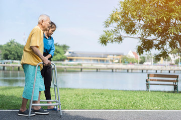 dramatic moments of young Asian carer assisting elderly or disabled using assistive walking...
